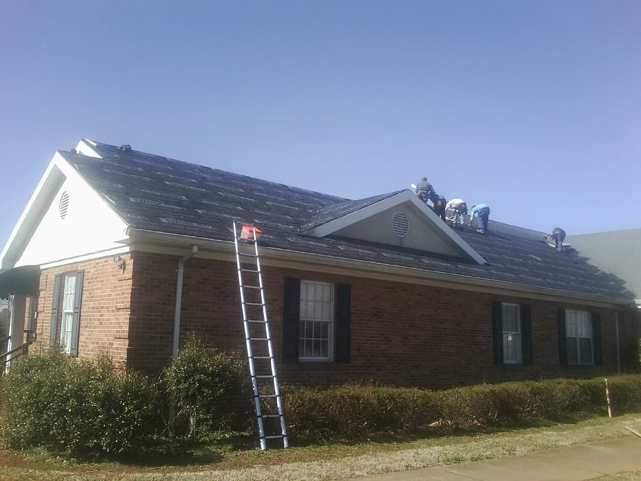 Crew tearing shingles off a brick ranch roof with a ladder set — Metal Roof Repair work by our crew in Orange Beach