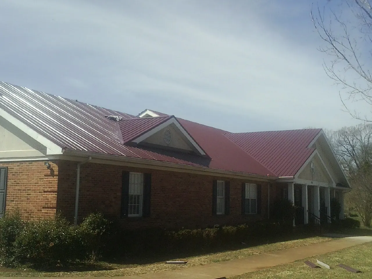 Red metal roof with gabled entries on a long brick building, from a Hail Damage Roof Repair job in Orange Beach