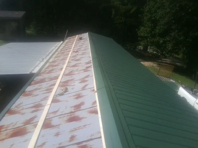 Old rusted panels beside newly installed green metal roofing — Wind Damage Roof Repair by Roofing Brothers in Orange Beach