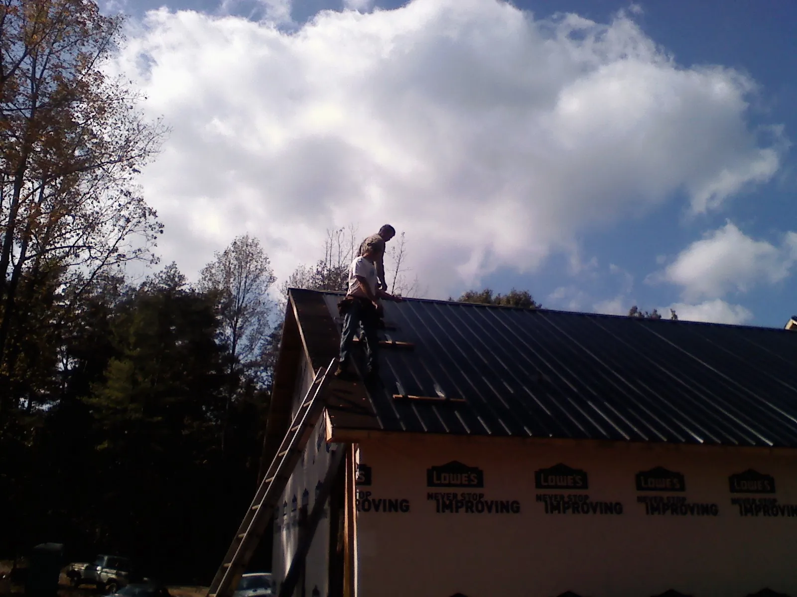 Roofer fastening dark metal panels high against a cloudy sky, from a Roof Inspection job in Orange Beach