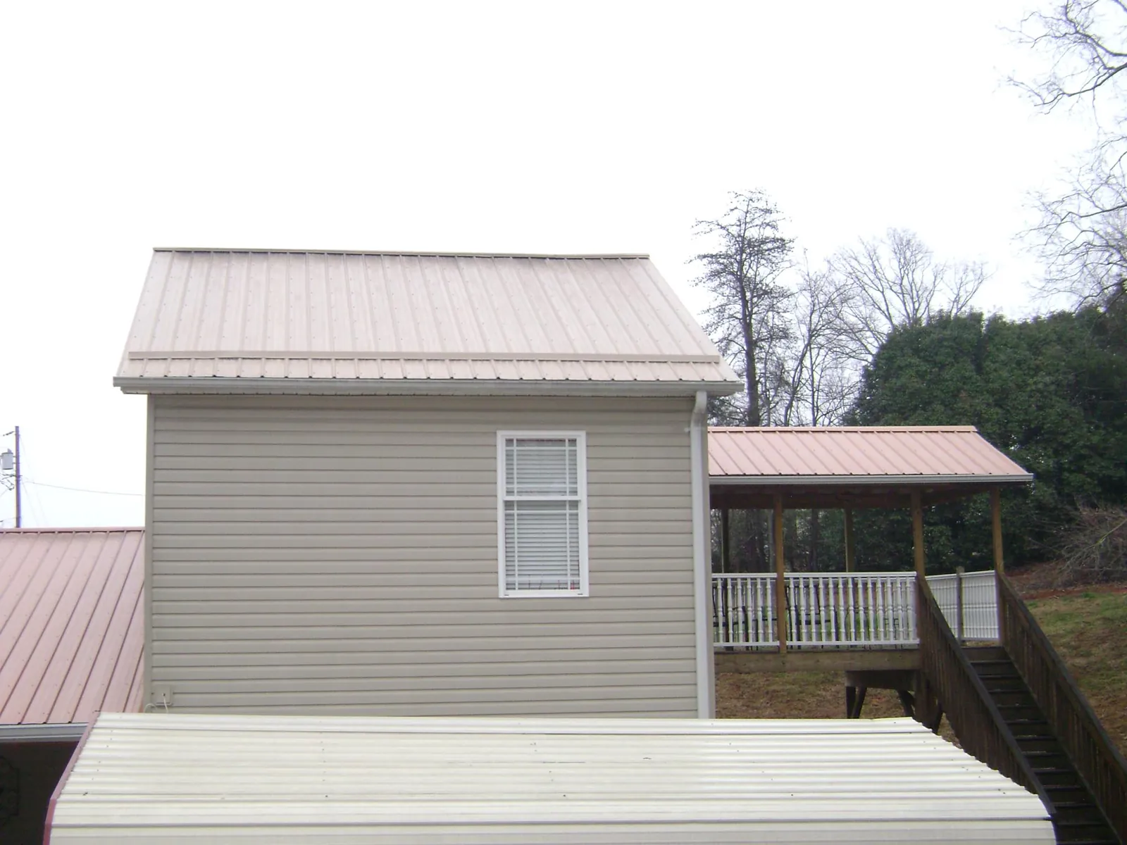 Tan metal roofs on a two story addition and attached porch, from a Roof Replacement job in Orange Beach